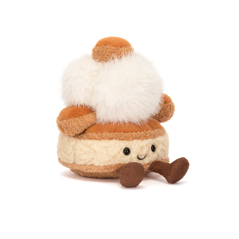 Jellycat St. Honoré cake shaped plush with a smiling face and brown feet on a white background. 
