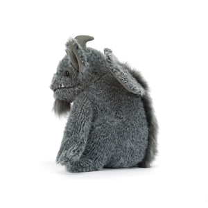 Side view of a gray plush gargoyle toy with large pointed ears, fangs, small horns, a stitched smiling face with a gray beard and a fur stripe down it's back. The plush is shown against a white background.