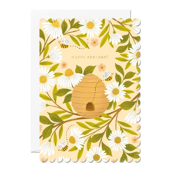 Greeting card with a scalloped edge featuring an illustration of bees and a beehive sitting on a tree branch surrounded by flowers. The text 'Happy Bee-day!' is printed over the bee hive on a light yellow background. 