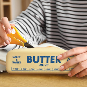 Image of a person taking scissors from a yellow pouch in the shape and style of a stick of butter. The text 'Butter me up' is printed on it, along with 'Salty & Sweet', 'Grade AA stuff' and some measurements. 