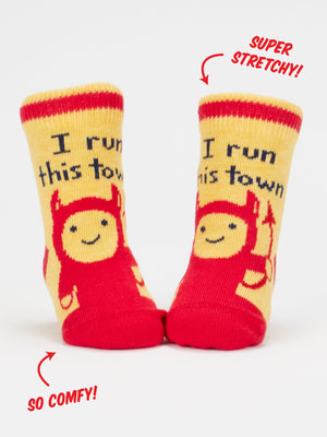 A pair of yellow socks featuring a print of a red devil character and the text 'I run this town'. The socks sit on a white background and are labelled with the text 'Super Stretchy!' and 'So Comfy'.