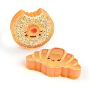Two smiling bread-themed kitchen sponges on a white background. One is in the style of a croissant, while the other is a bagel with a bite taken from it. 
