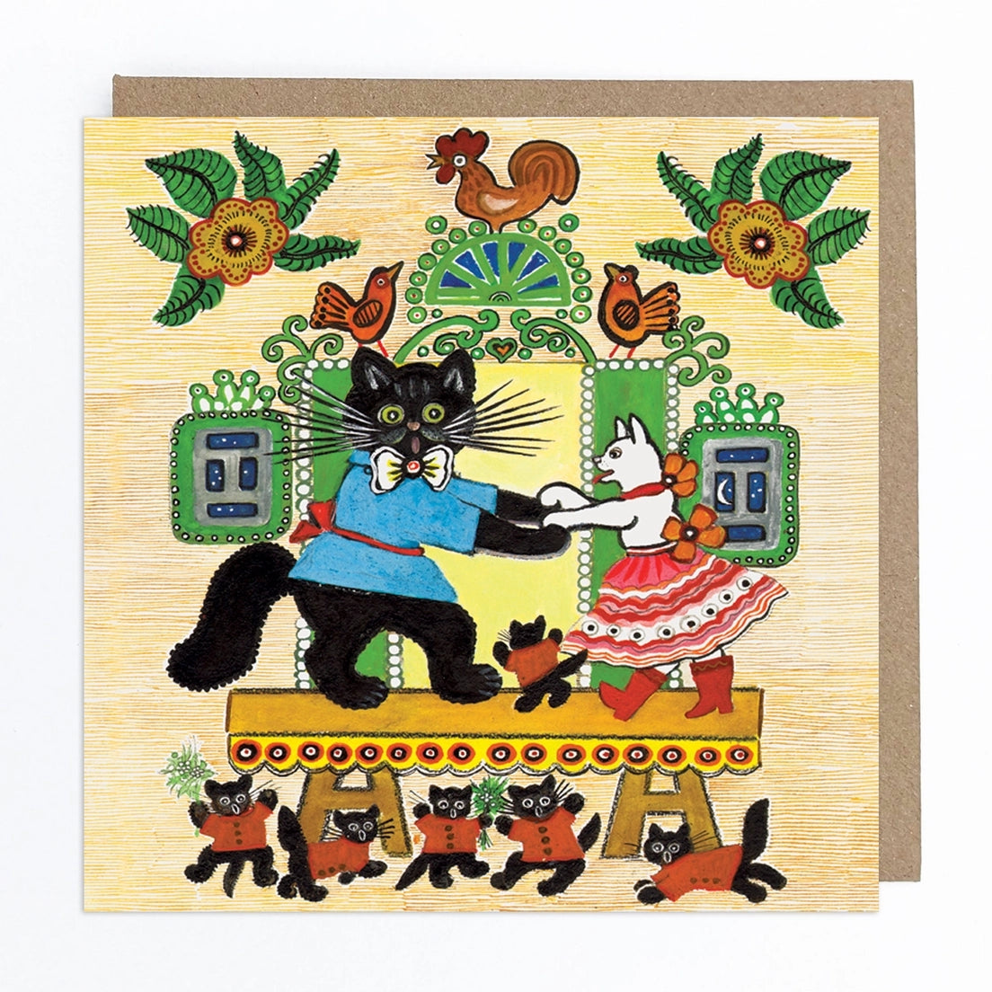 Greeting card featuring a folk art style illustration of a black cat wearing a blue shirt, red belt and bow tie dancing with a white cat wearing a red and white skirt, red boots, and a flower around it's neck. They both stand on top of a yellow stage, along with a smaller black cat wearing a red shirt. Below the stage, five more black cats wearing red shirts stand. Behind the stage, a rooster and two birds perch over a door and windows with green shutters along with two abstract flowers in each corner. 