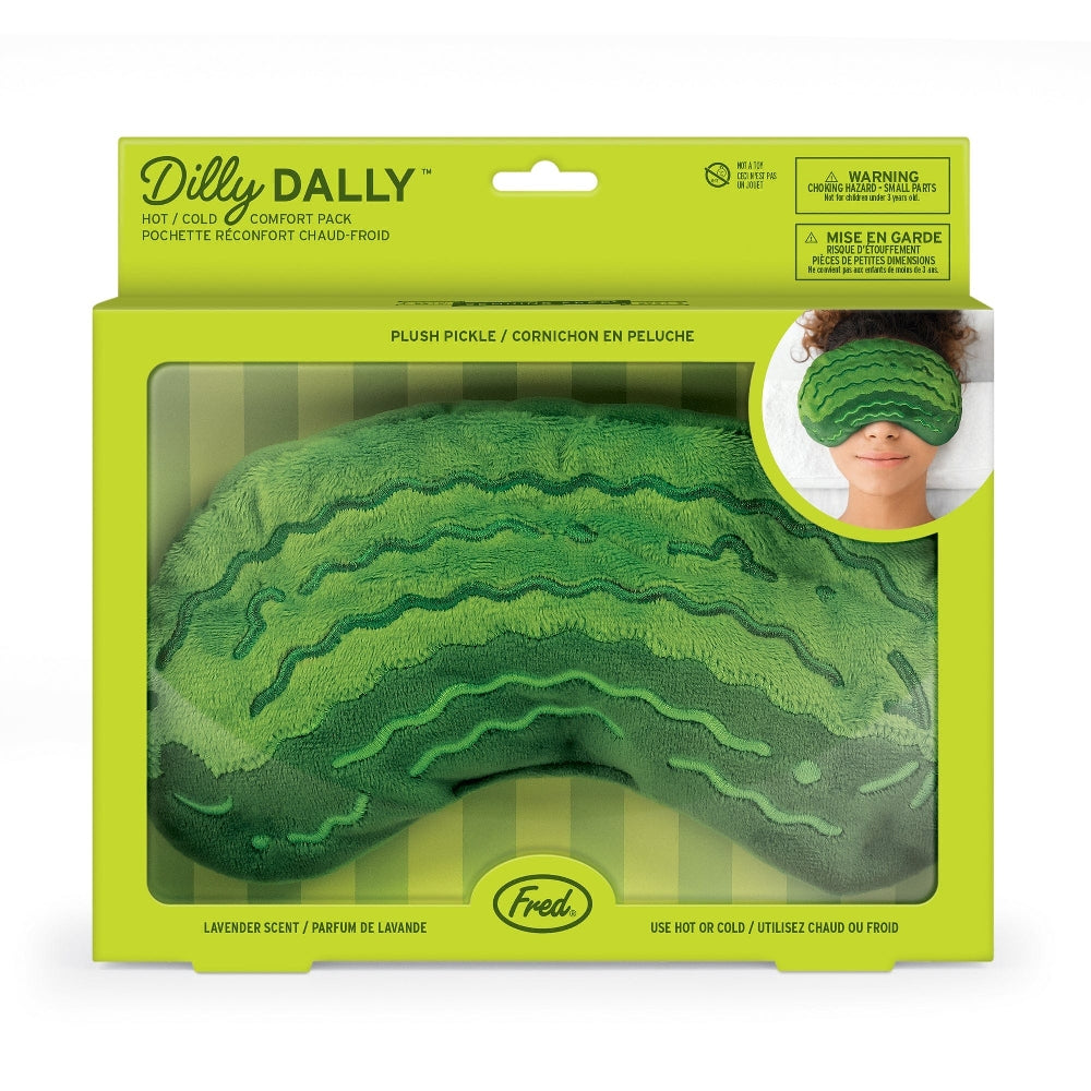 Green plush pickle-shaped comfort eye mask in its green packaging box, with the company branding and the text 'Dilly Dally'. An image of a woman wearing the mask over her eyes is pictured in the top right corner. The product is shown on a white background. 