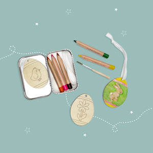 Open packaging featuring wooden Easter themed templates and colored pencils on a light blue background,