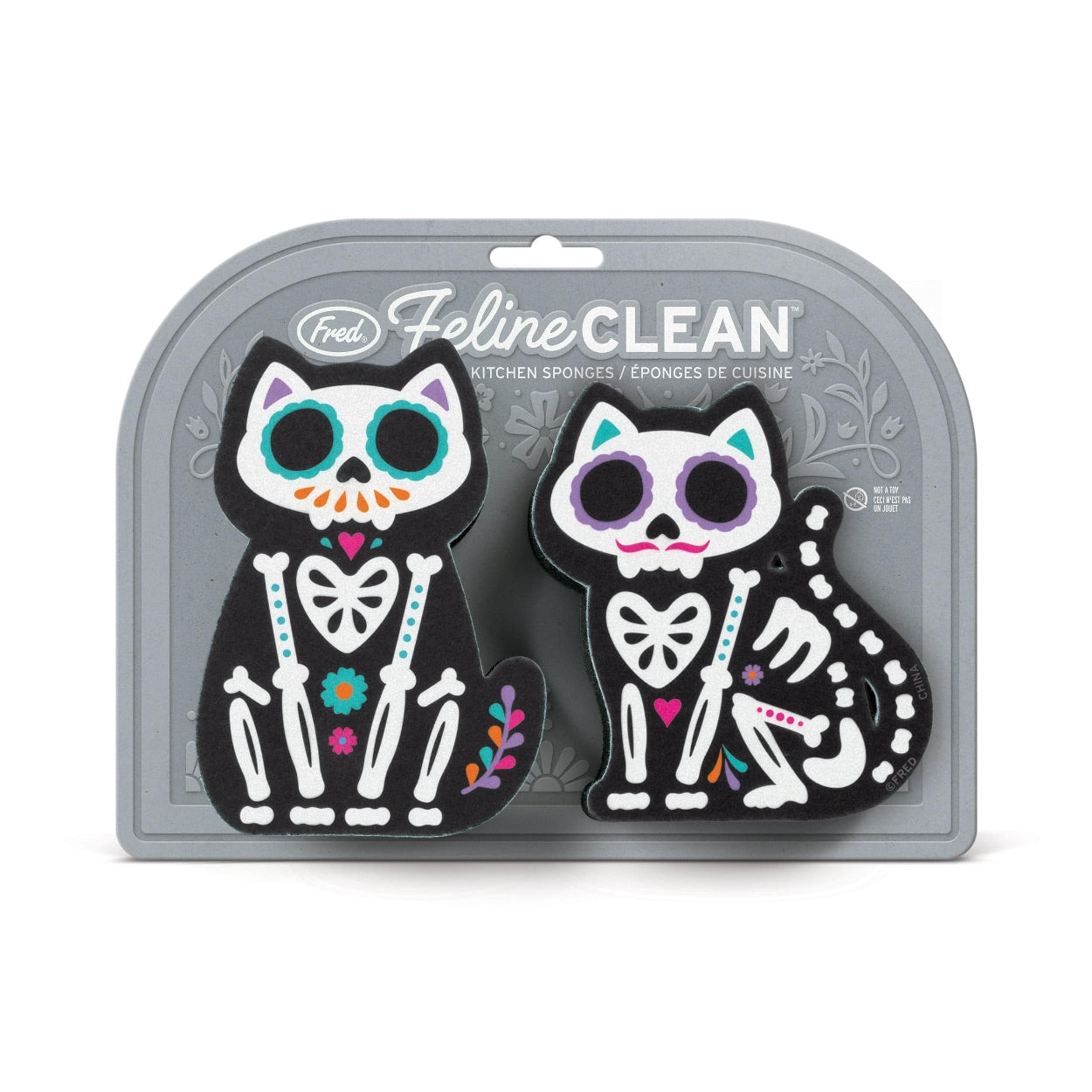 Image of two sugar skull cat-themed kitchen sponges attached to their packaging. The packaging is grey with the text 'Feline Clean' and the company branding and sits on a white background.