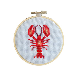 Cross-stitched lobster design contained in a wooden embroidery hoop on a white background.