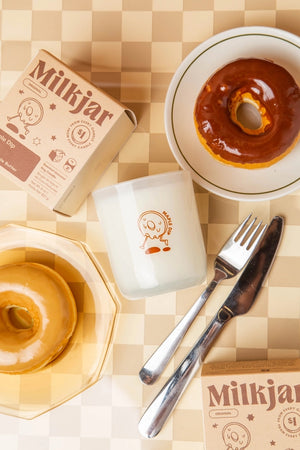 Donuts with glaze, a white candle, and 'Milkjar' packaging on a checkered tablecloth.