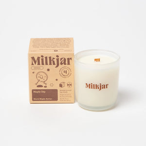 White candle with brown text saying 'Milkjar', beside a box with brown Milkjar branding on a white backgroud.