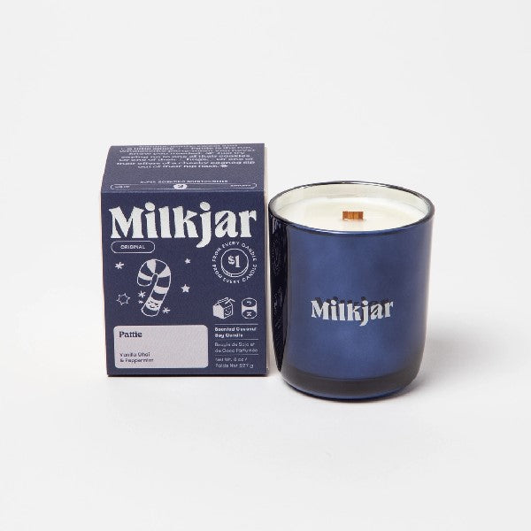 Canadian company Milkjar candle and its box packaging. The white candle is in a dark blue glass with "Milkjar" written in grey. The other side of the candle has a cute smiling candy cane doodle in grey. The packaging is a small dark blue box with grey text and graphics. 