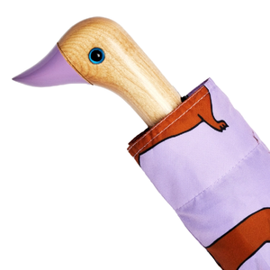 Closeup of the top half of a purple umbrella with an abstract weiner design and a wooden duck head shaped handle on a white background. 