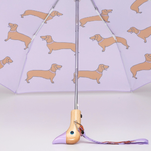 Open view of a purple umbrella with an abstract weiner design and a wooden duck head shaped handle on a white background. 