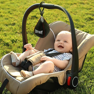 Baby sitting in a stroller with a 'Buff Baby' product attached, outdoors on grass.