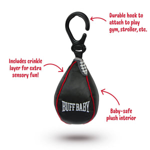 The image shows a black punch bag shaped hanging baby toy attached to a clip. A red tag in the shape of a boxing glove shows the company branding and text 'Buff Baby'. The hanging toy sits on a white background. Text beside the image 'Includes crinkle layer for extra sensory fun!', 'Baby-safe plush interior' and 'Durable hoolk to attach to play gym, stroller, etc.'