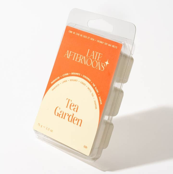 A packaged wax melt product with label that shows the brand name and the text 'Tea Garden' with a bright cream and orange color scheme. The package sits on a white background. 