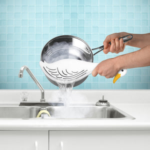 Image of a person holding a white duck-themed pot strainer as they use it to strain water from a pot over a sink. 