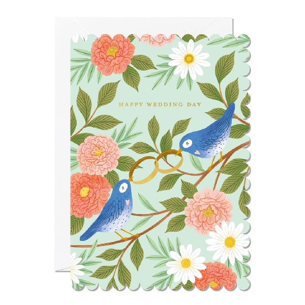 Greeting card with a scalloped edge featuring an illustration of two blue birds holding wedding rings in their beaks as they sit on the branch of a tree, surrounded by flowers. The text 'Happy Wedding Day' is printed over the birds. 